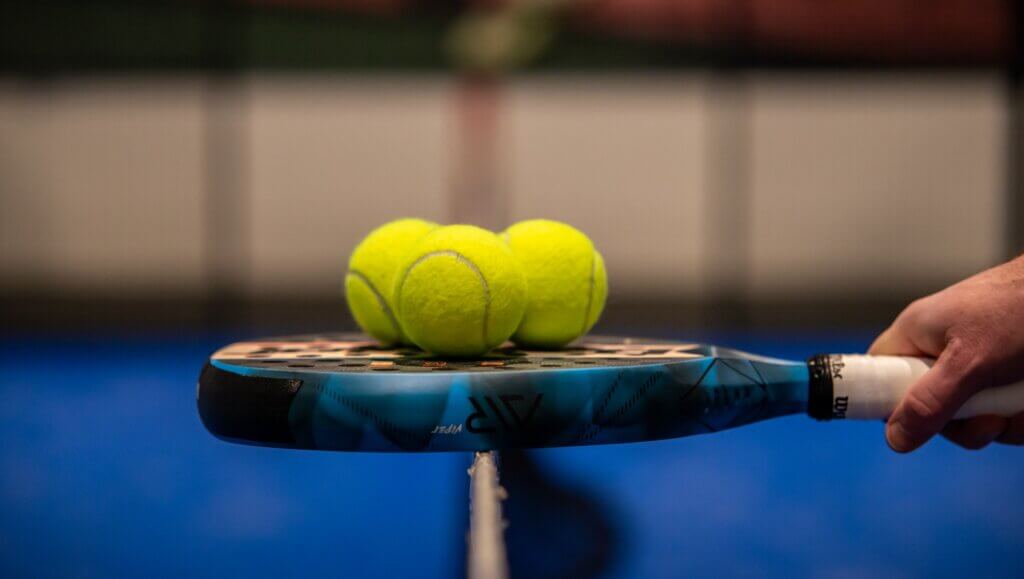 Macro or closeup photo of padel racket and a padel ball, a hand holding the racket